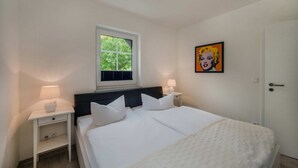 A bedroom with a bed, two bedside tables, a window, a door, and a painting on the wall.