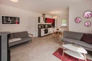 A modern apartment with a grey sofa, a dining table, a kitchen with red cabinets, and a small dining area. - Modern vacation apartment in Heringsdorf with a garden—close to the beach and (Heringsdorf)
