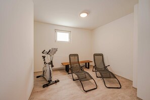 Una habitación con ventilador de techo, una bicicleta estática, una mesa de madera y dos sillones reclinables.