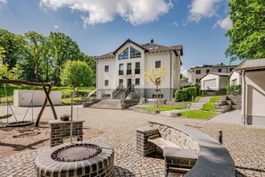 Un edificio moderno con un patio che include altalene, un braciere e una scalinata che conduce all'ingresso.