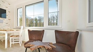 A room with two brown leather chairs, a wooden table, and large windows with a view of trees. - Modern bungalow in Heringsdorf with sauna, garden and close to the beach - Villa Doris (Heringsdorf)