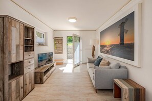 Una sala de estar moderna con una televisión, un sofá gris, un aparador de madera y un cuadro grande de un faro.
