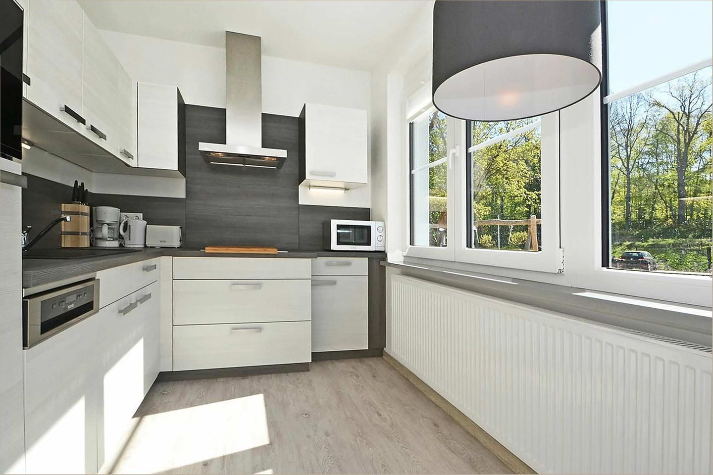 A modern kitchen with white cabinets, a built-in microwave, a coffee maker, and a window with a view of trees.