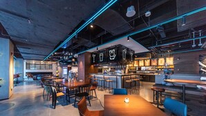 Un espace bar moderne avec un panneau néon, des tables en bois et des tabourets de bar.