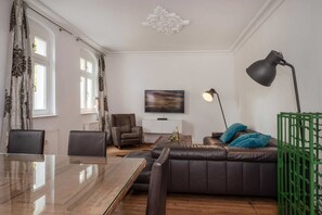 A modern living room with a glass dining table, leather sofa, and a TV mounted on the wall.