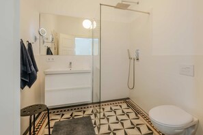 Un baño con cabina de ducha de vidrio, un lavamanos blanco, un inodoro y un suelo estampado.