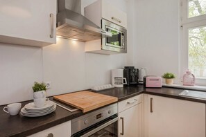 A modern kitchen with a microwave, coffee maker, toaster, and wooden cutting board.