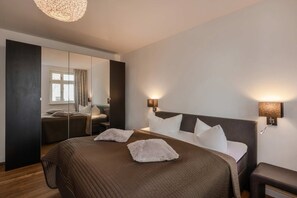 Habitación de hotel moderna con una cama grande, lámparas de noche, un espejo y vistas al exterior.