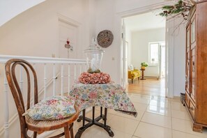 Ein Zimmer mit einem Holzstuhl, einem Tisch mit Blumenmuster-Tischdecke, einem Glasbehälter und einem Holzschrank.