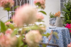 Uma mesa com toalha estampada, um busto e um vaso com flores secas.
