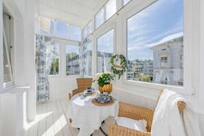 A sunlit room with a table set for two, a wicker chair, and a view of buildings through large windows. - Vacation apartment "Seewind" - Stylish time out near the beach & Baltic Sea on Usedom - (Heringsdorf)