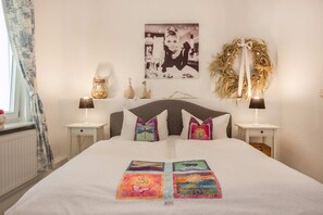 Ein ordentlich eingerichtetes Schlafzimmer mit einem Bett, zwei Nachttischen, einem Wandbild und einem dekorativen Kranz.