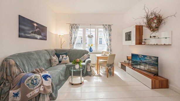 A living room with a sofa, a coffee table, a TV, a dining area, and a window with curtains. - "Seeadler" Vacation Rental – A Baltic Sea Getaway in Heringsdorf, 200 m from the beach - (Heringsdorf)
