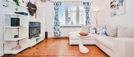 Un salon moderne avec un canapé blanc, un téléviseur et un plancher en bois.
