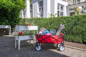 A red cart with sports equipment parked next to a white bench and a hedge.