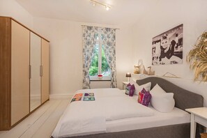 A bedroom with a bed, a wardrobe, a window with curtains, a bedside table, and a wall-mounted picture.