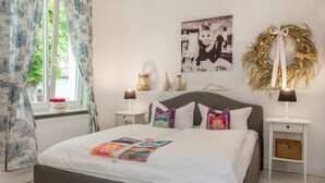 A neatly arranged bedroom with a bed, two bedside tables, a window with curtains, a wall-mounted picture, and a decorative wreath. - "Seeadler" Vacation Rental – A Baltic Sea Getaway in Heringsdorf, 200 m from the beach - (Heringsdorf)