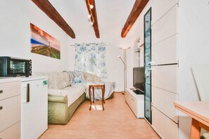 Eine kompakte Küche mit Sofa, kleinem Tisch, Mikrowelle und Fernseher.