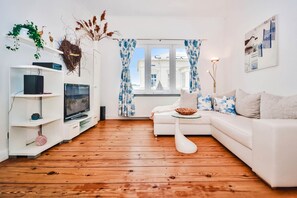 Ein modernes Wohnzimmer mit einem weißen Sofa, einem Fernseher und Holzboden.