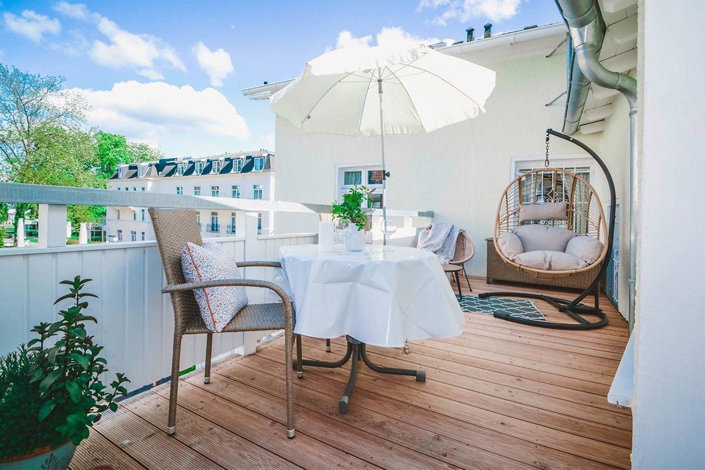 A wooden deck with a table and chairs, a hanging chair, and a white umbrella.