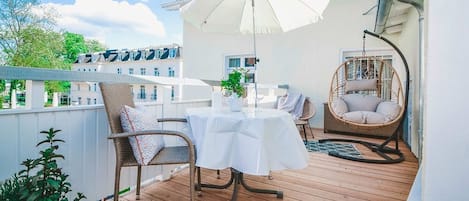 A wooden deck with a table and chairs, a hanging chair, and a white umbrella.