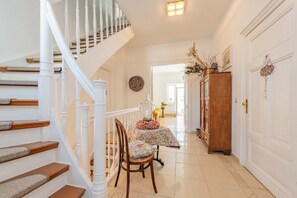 A staircase with white balusters, a wooden chair with a floral cushion, and a table with a floral tablecloth.