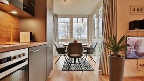 A modern kitchen with a dining area, a large window, and a potted plant. - Bädervilla am Höppnerweg Apartment 5 - Bädervilla am Höppnerweg (Timmendorfer Strand)