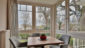 A conservatory with a table and four chairs, a red bowl with a plant, and a view of trees and buildings outside. - Bädervilla am Höppnerweg Apartment 5 - Bädervilla am Höppnerweg (Timmendorfer Strand)