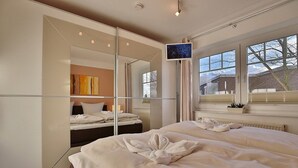 A modern hotel room with two beds, a large mirror, a television, and a view of the outside. - Bädervilla am Höppnerweg Apartment 5 - Bädervilla am Höppnerweg (Timmendorfer Strand)