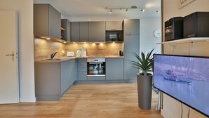 A modern kitchen with grey cabinets, a built-in oven, and a wooden countertop. There is a potted plant and a flat-screen TV mounted on the wall. - Bädervilla am Höppnerweg Apartment 5 - Bädervilla am Höppnerweg (Timmendorfer Strand)