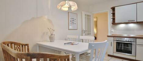 A dining area with a white table and chairs, a hanging light fixture, and a kitchen with white cabinets and an oven.
