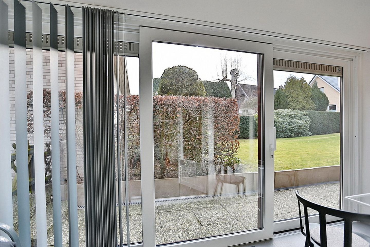 Una habitación con una puerta corrediza de vidrio que da a un patio con vistas a un jardín y un seto.