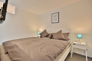 Una cama bien hecha con edredón marrón y almohadas, dos mesitas de noche con lámparas, y una cita inspiradora enmarcada en la pared.