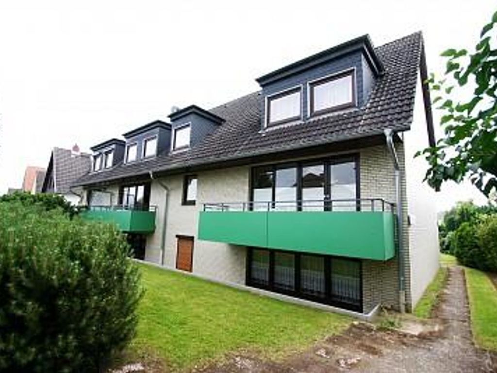 Une maison moderne à deux étages, dotée d’un toit en pente, de grandes fenêtres et d’un auvent vert au-dessus de l’entrée.