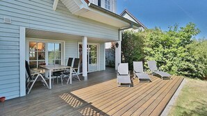 A house with a covered patio, a dining area with a table and chairs, and a deck with lounge chairs. - Vacation cottage Spitsbergen (Timmendorfer Strand)