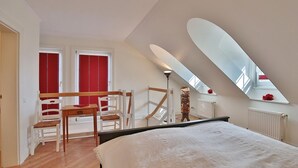 A bedroom with a large bed, a wooden chair, a desk, and a red-framed window. - Vacation cottage Spitsbergen (Timmendorfer Strand)
