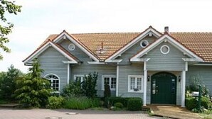 A two-story house with a tiled roof, a front entrance with a green door, and a paved driveway. - Vacation cottage Spitsbergen (Timmendorfer Strand)