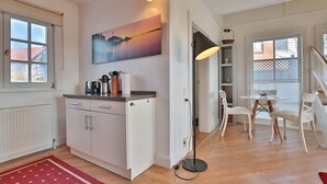 A modern kitchen with white cabinets, a red rug, and a painting of a sunset. - Vacation cottage Spitsbergen (Timmendorfer Strand)