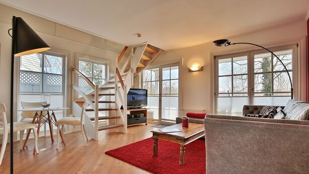 A spacious living room with a wooden staircase, a television, and a red rug. - Vacation cottage Spitsbergen (Timmendorfer Strand)