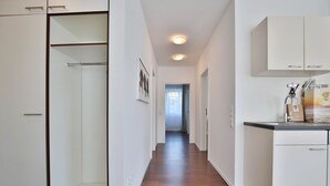 A narrow hallway with wooden flooring, white walls, and a kitchen area with cabinets and a countertop.