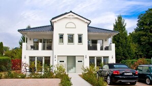 A two-story white house with a balcony, a garage, and a driveway with two cars parked.