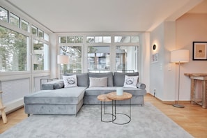 A modern living room with a sectional sofa, a round coffee table, and large windows offering a view of the outside.