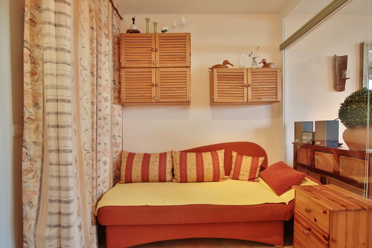 Une chambre à coucher avec un lit, une armoire en bois, un miroir et une fenêtre avec des rideaux.