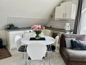 A modern kitchen with white cabinets, a dining table with chairs, and a coffee machine.
