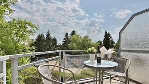 Ein Balkon mit Glastisch, zwei Korbstühlen, einer Weinflasche und einem Blumenstrauß.