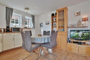 A compact living space with a dining area, kitchenette, and a TV. - Haus Parkblick Apartment 4 - Haus Parkblick, Timmendorfer Strand (Timmendorfer Strand)