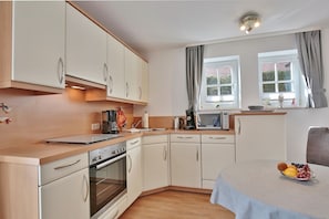 A compact kitchen with white cabinets, a built-in oven, a microwave, and a coffee maker. There is a dining table with a fruit bowl on it. - Haus Parkblick Apartment 4 - Haus Parkblick, Timmendorfer Strand (Timmendorfer Strand)