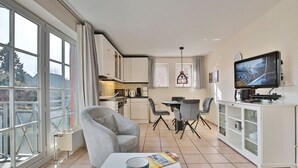 Eine moderne Küche mit weißen Schränken, einem Essbereich mit Tisch und Stühlen, einem Fernseher und einem großen Fenster.