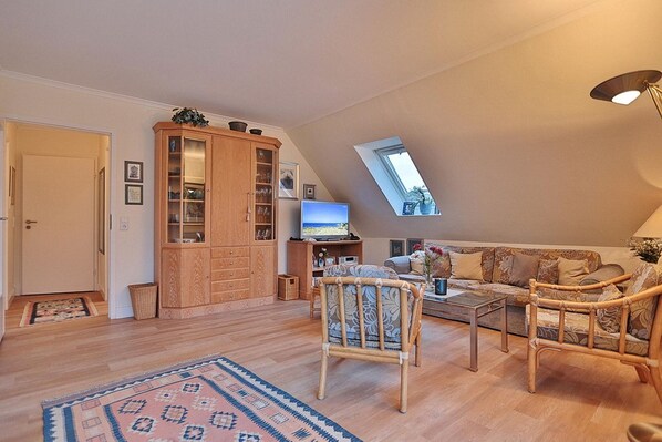 A cozy loft-style living room with a high ceiling, a built-in wooden cabinet, a television, a sofa, and a coffee table.
