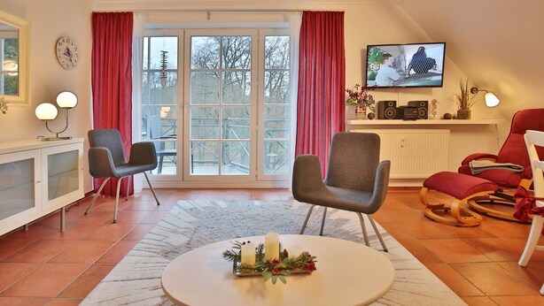 A living room with a large window, two armchairs, a red sofa, a television, and a small table with candles. - Haus Parkblick Apartment 10 - Haus Parkblick, Timmendorfer Strand (Timmendorfer Strand)